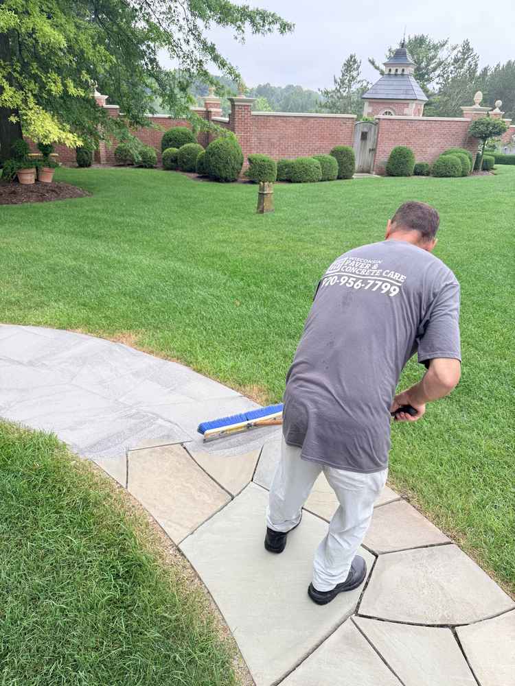 Worker applying sealant to concrete pavers along a walkway in front of brick wall and manicured lawn in Fond du Lac, Wisconsin