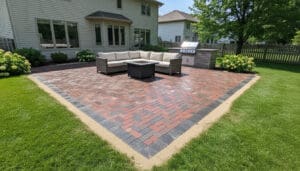Brick paver patio with sectional seating, fire pit table, and built-in grill in residential backyard