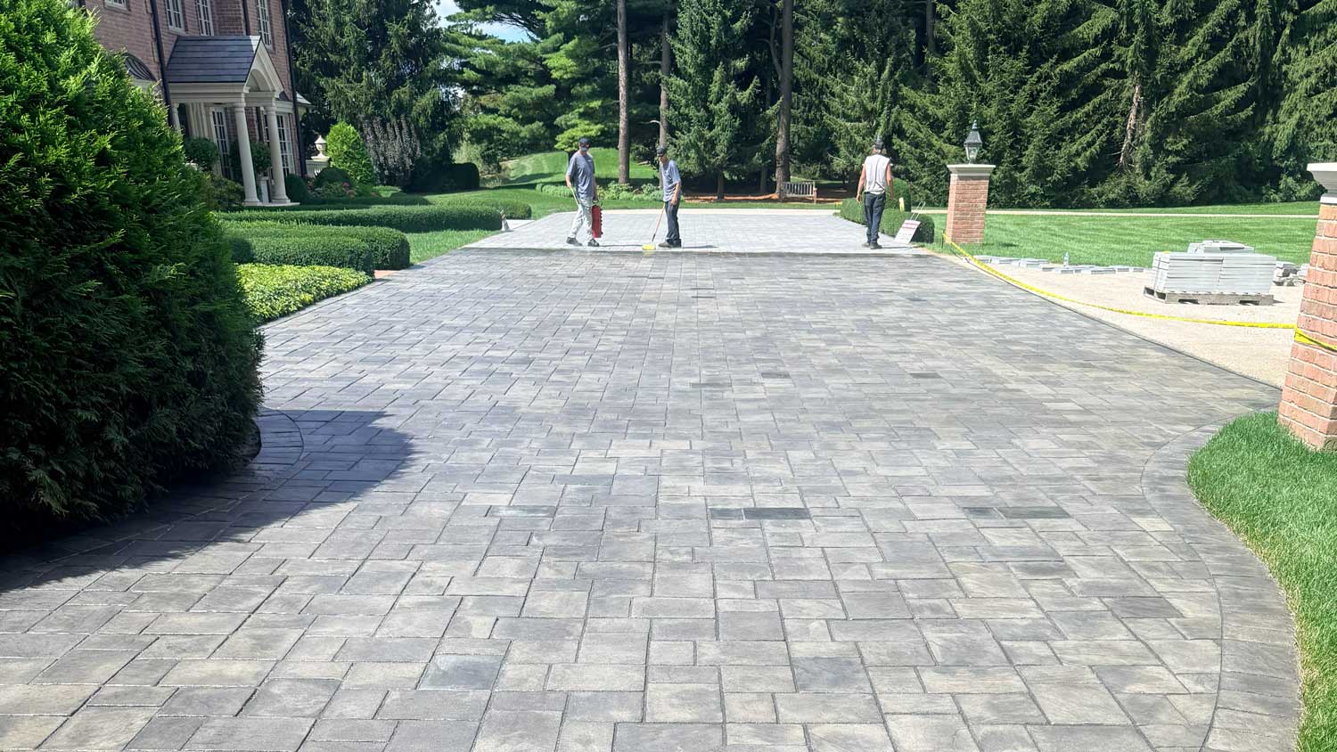Newly installed gray paver driveway with herringbone pattern in residential Cincinnati, Ohio property with manicured landscaping and workers in background