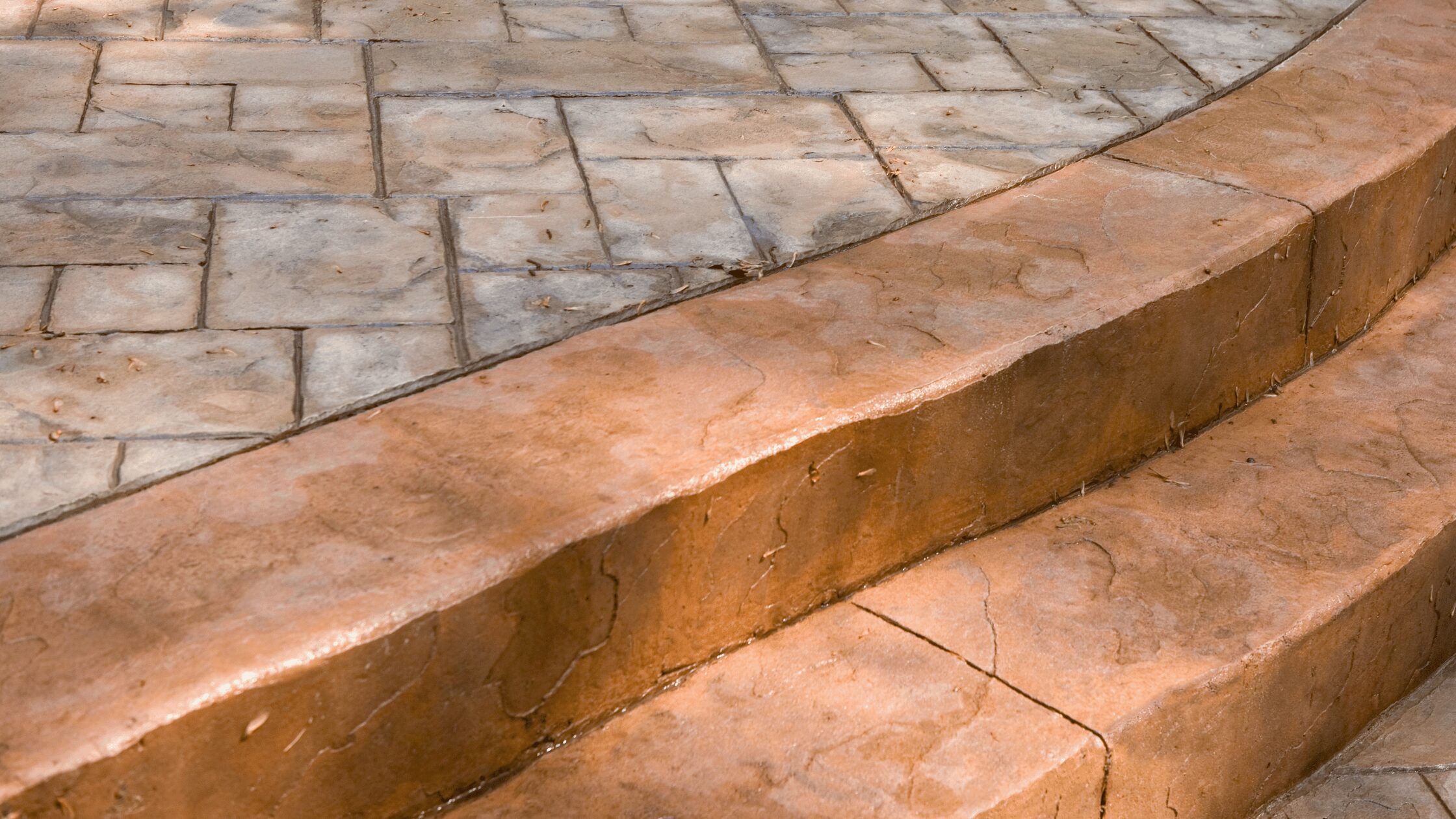 Close-up of concrete paver steps showing terracotta and gray stamped pavers with visible wear, ideal for paver restoration and sealing services